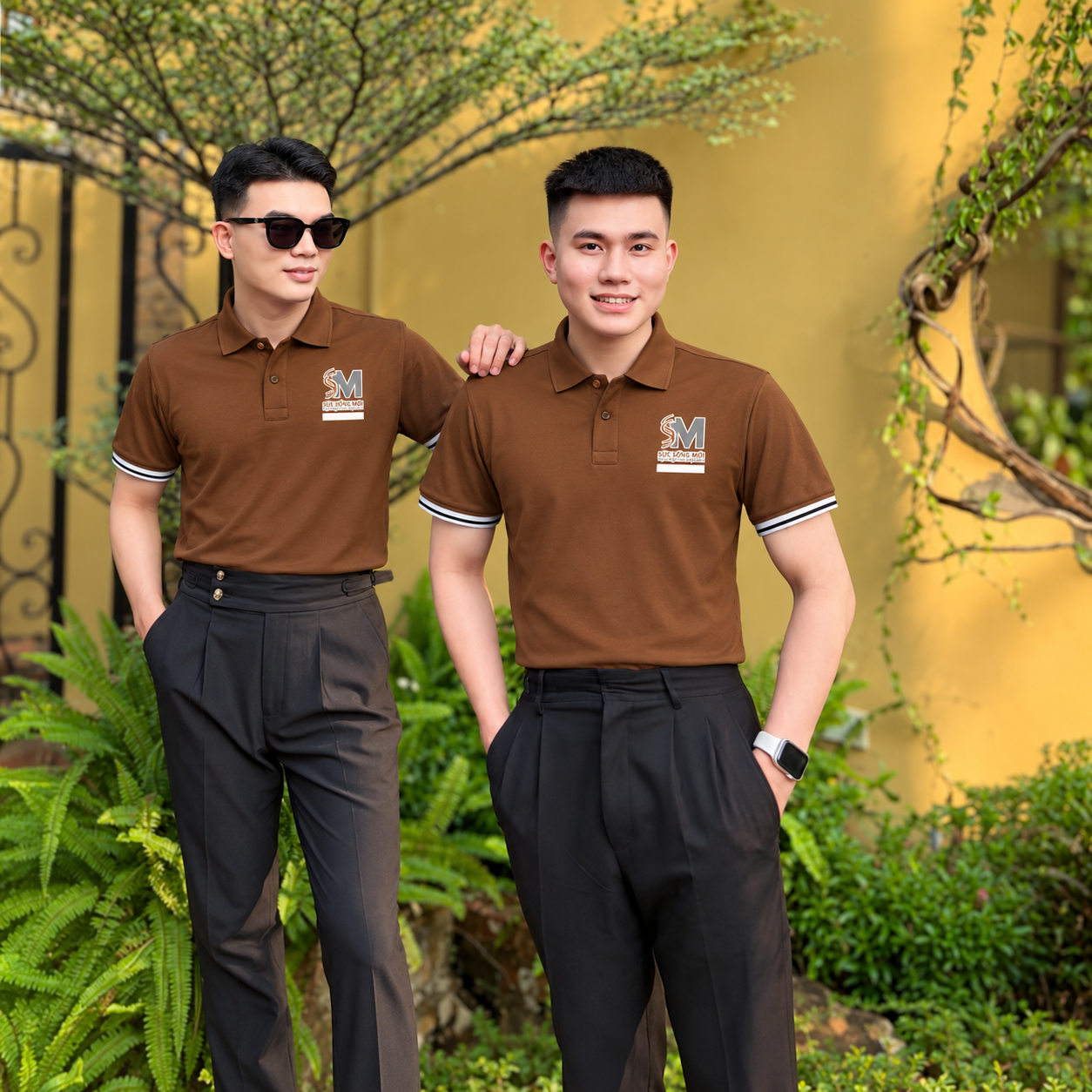 Hai nhân viên mặc áo polo đồng phục nâu Sức Sống Mới phối cùng quần đen