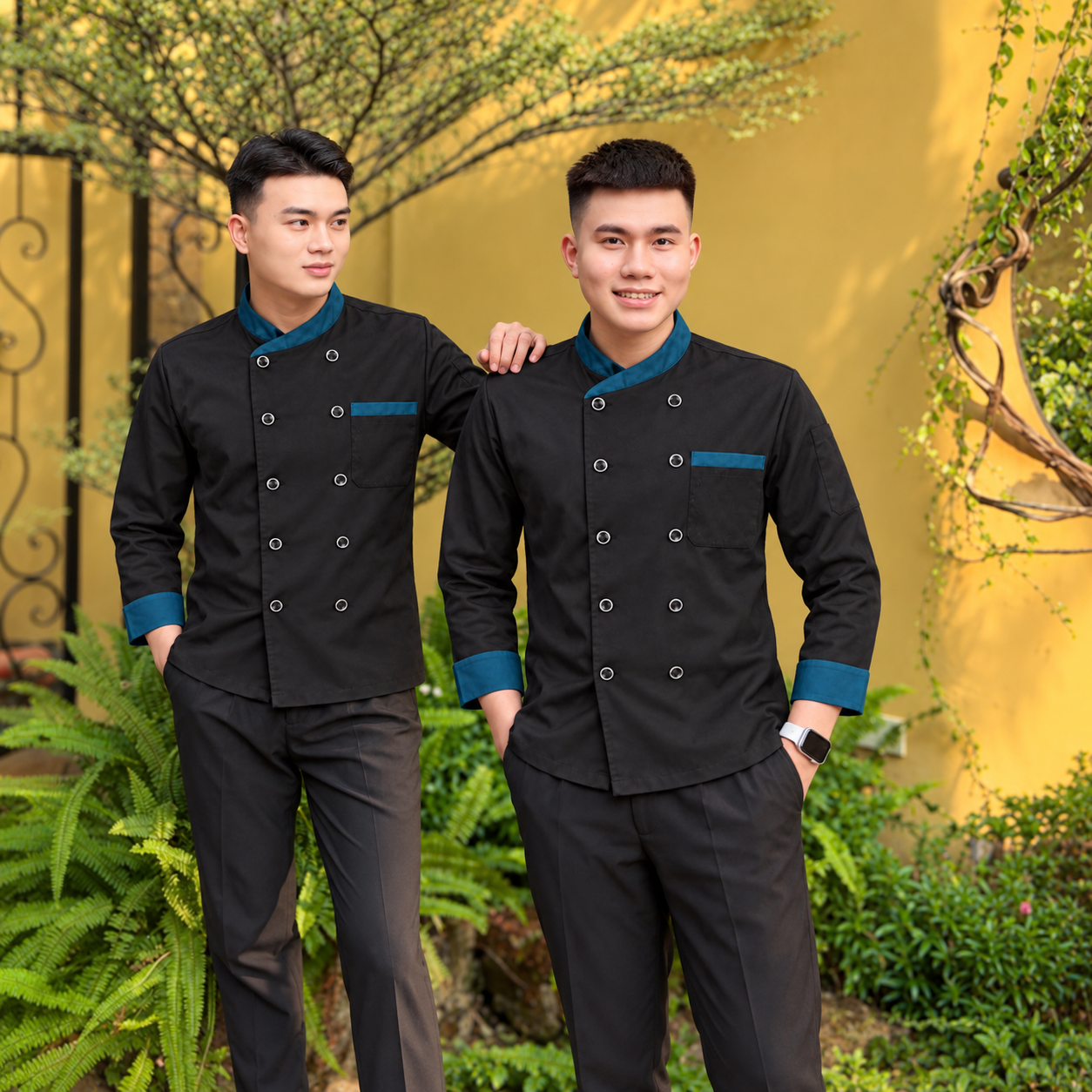 Người mẫu nam mặc áo đầu bếp đen tay dài phối xanh, hai hàng nút bạc và quần đen