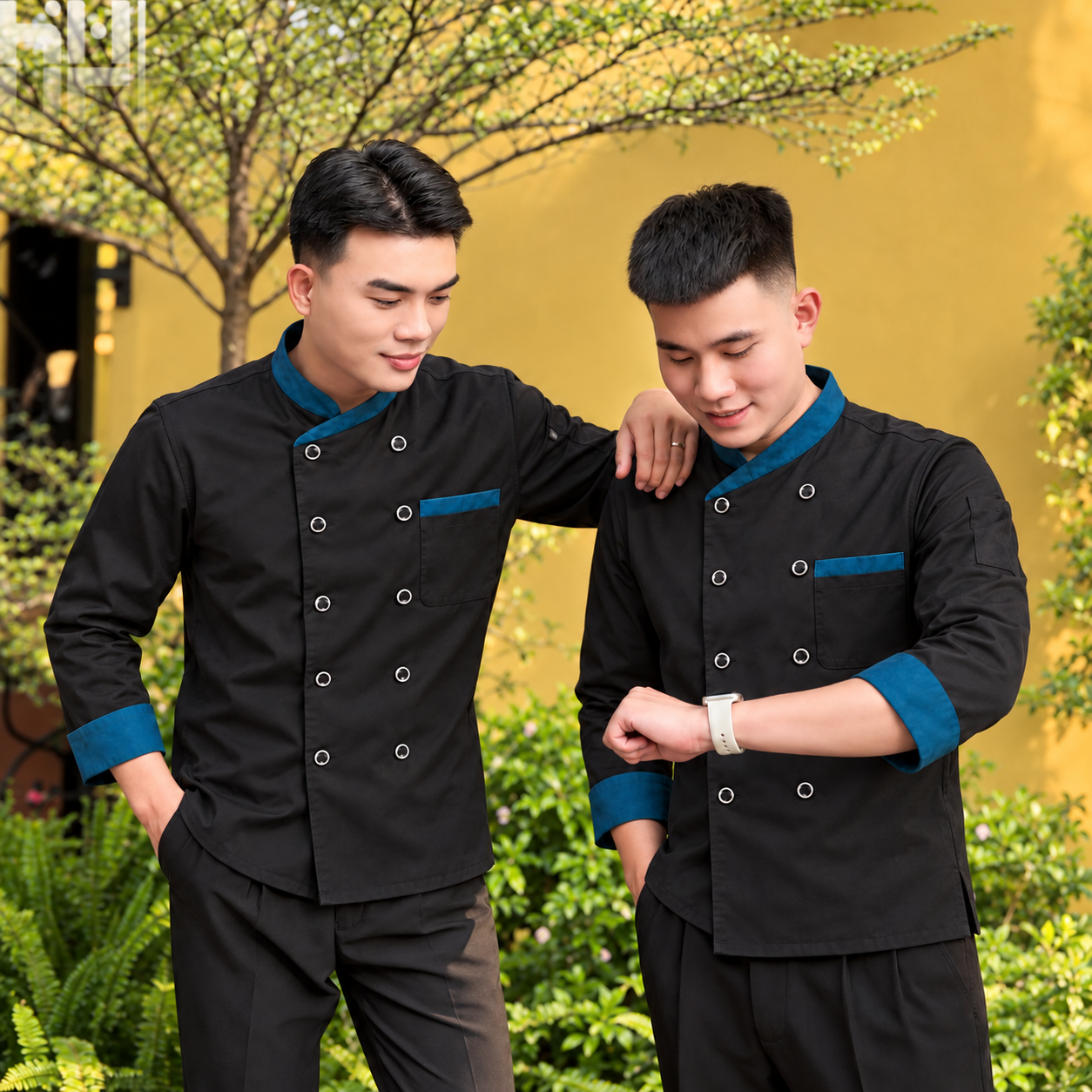 Hai người mẫu nam mặc áo đầu bếp đen phối xanh với quần đen