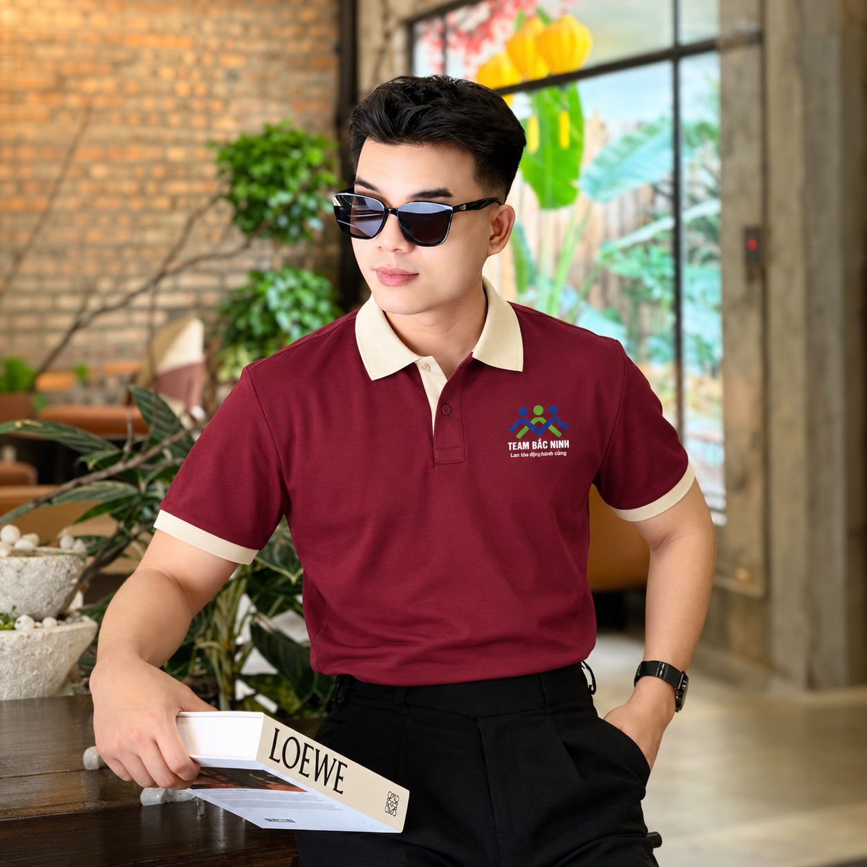 Người mẫu nam mặc áo polo đỏ đô phối kem Team Bắc Ninh kết hợp quần tây đen